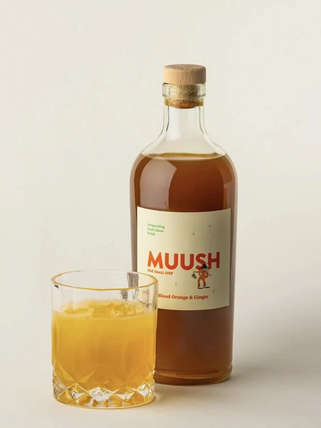 Blood Orange & Ginger Elixir, a drink sitting on a plain surface next to a bottle. 