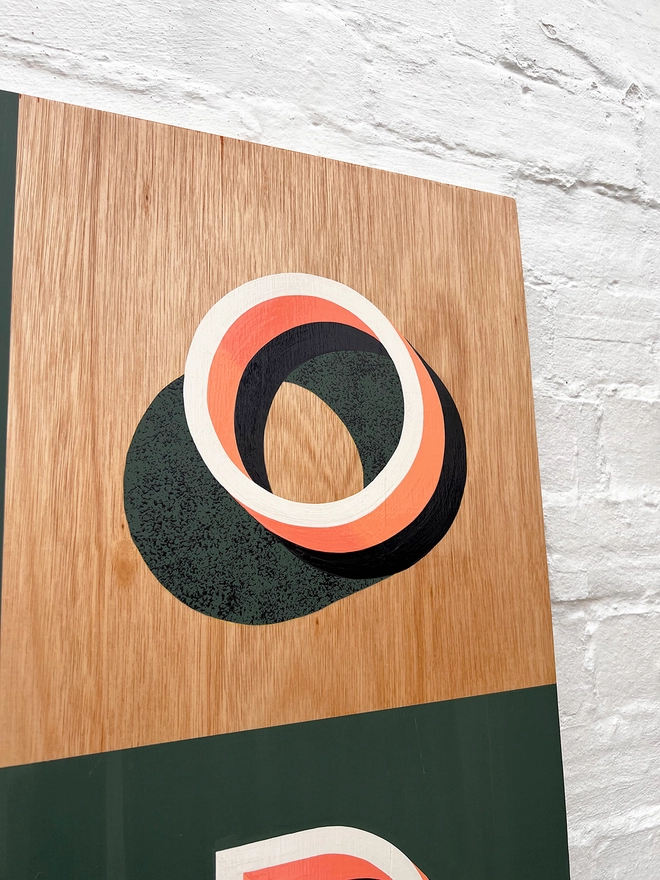 Close up of the letter O from FOOD hand painted sign in coral, green and aubergine, against a white brick wall, at an angle. 