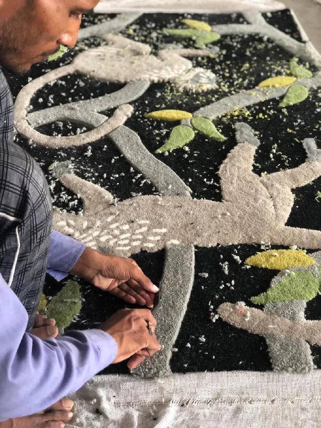 A person hand trimming a Langur monkey tufted rug.