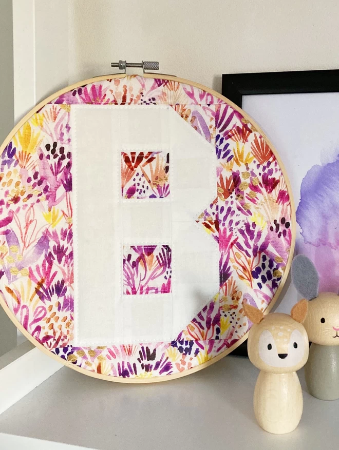 Personalised quilted hoop against a pink and purple floral background with the letter 'B' in white.