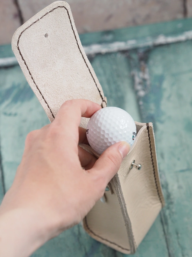 Handmade leather golf ball holder. Natural cream leather golf ball case showing a hand placing a golf ball inside.