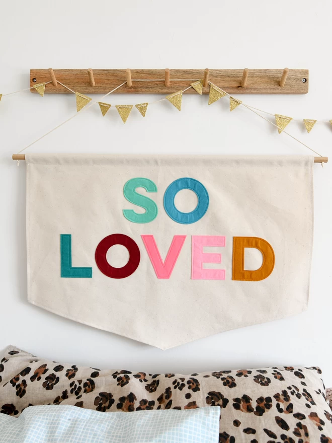 Canvas banner with the words so loved appliquéd on in colourful felt letters.