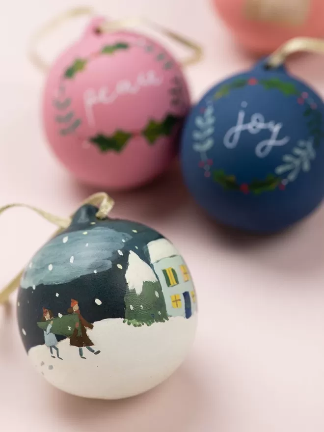 Personalised christmas baubles handpainted, two with names and one with an illustration of people walking to home in the snow