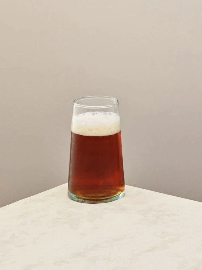 Highball Glasses (Set Of 1 Or 4), a highball glass sitting on a plain counter top against a white backdrop. It is filled with a soft drink. 