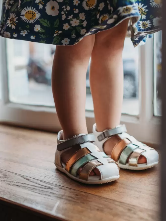 Little girl wearing a floral dress and Pip and Henry blue metallic gladiator sandals