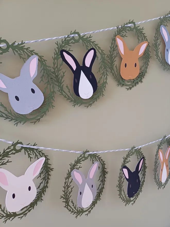 Easter Bunny Garland (12 bunny option) displayed on green wall. Bunny decorations alternate between rabbits with white noses and rabbits solid colour face 