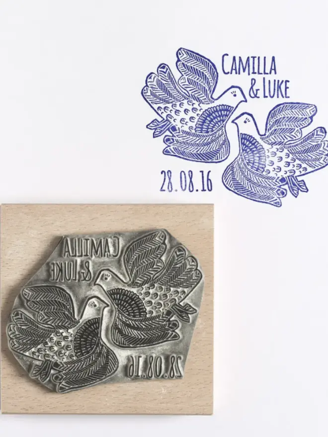 Wooden lino cut rubber stamp with two illustrated love birds and the text ‘Camilla & Luke’ and the date ‘28.08.16’, shown next to a blue ink stamp impression on white paper.