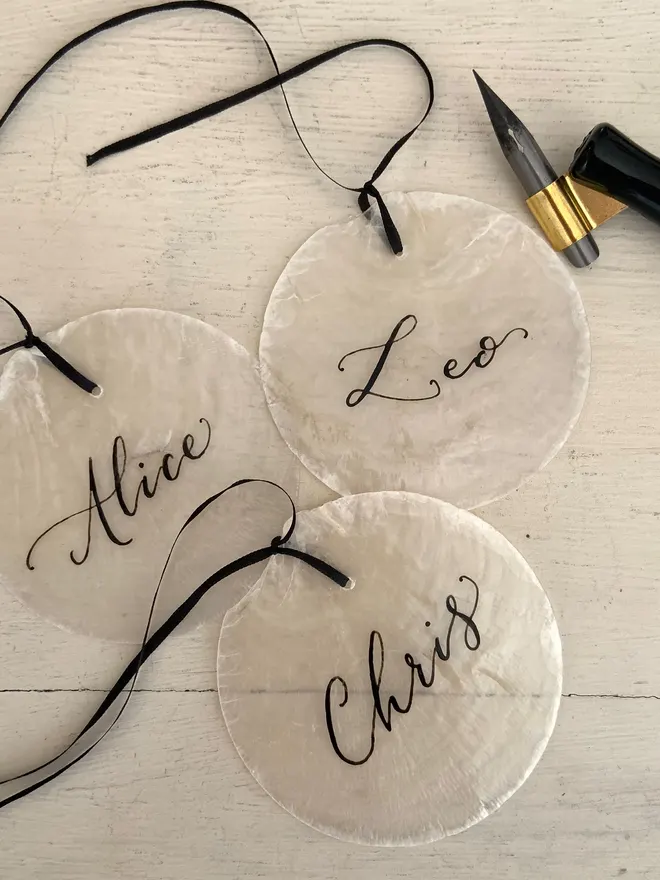 Capiz shell wedding place cards. Round discs of natural capiz shell with your guests names hand scripted in black ink ribbon. Can have narrow ribbon attached for a finishing touch