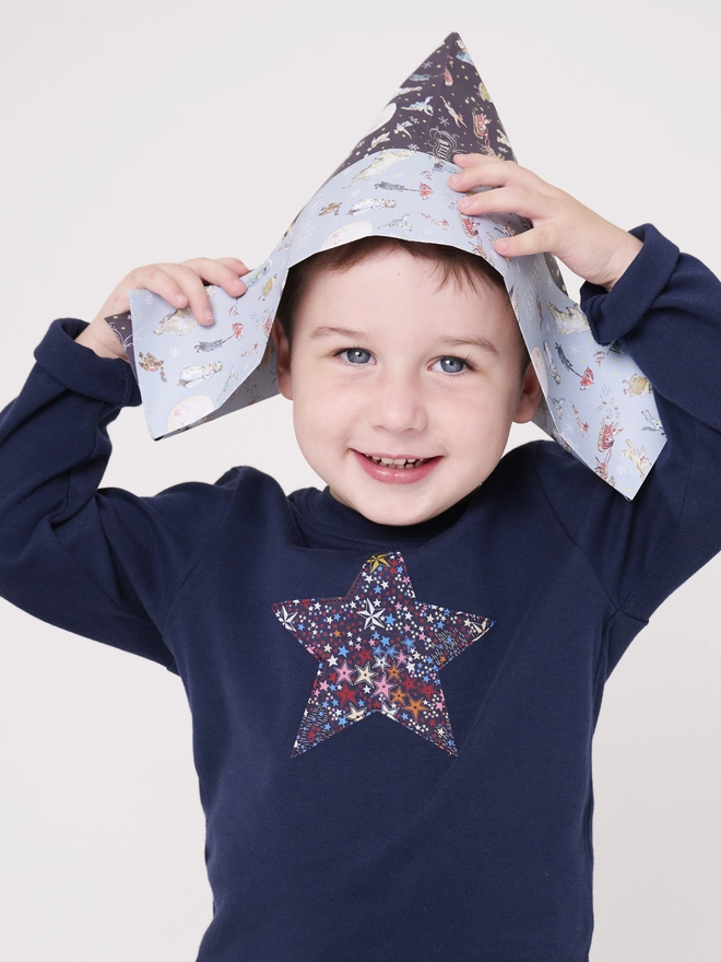 A little boy wearing a navy blue christmas tee with a Liberty star print star sewn on the front