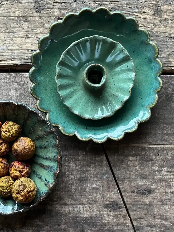 Handmade Green Ceramic Candlestick Holder, a pair of green candlestick holders sitting on a wooden surface. They are accompanied by a bowl of fruit. 