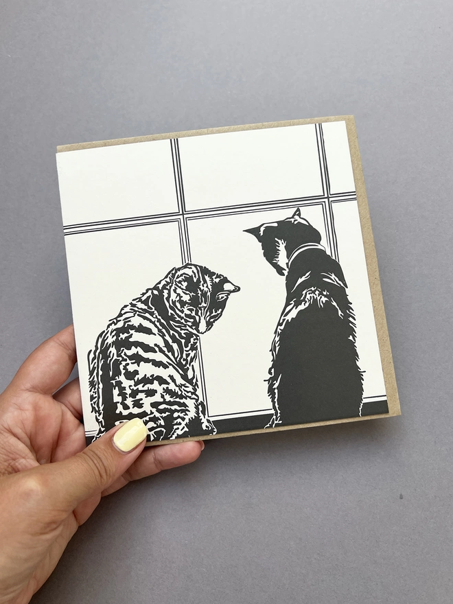 Hand holding the Window time card which is a tabby cat and a black and white car sat in front of a sash window 