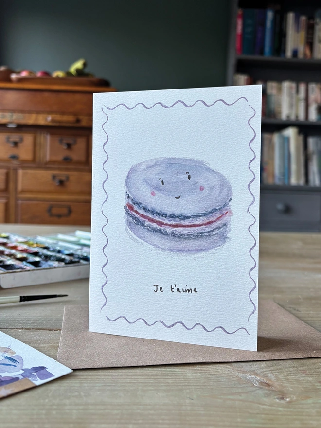 Chic Valentine's Day Card featuring a hand painted Macaron with a smiling face.  The Card reads Je t'aime which means I Love You