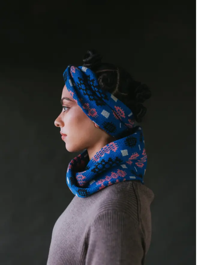 Model wearing pieces from MABLI's 'Carthen' collection, featuring the Carthen Wrap in the vibrant 'Klein blue/Rhosyn' colour-way. The design showcases bold, colourful patterns inspired by traditional Welsh blanket tapestry.