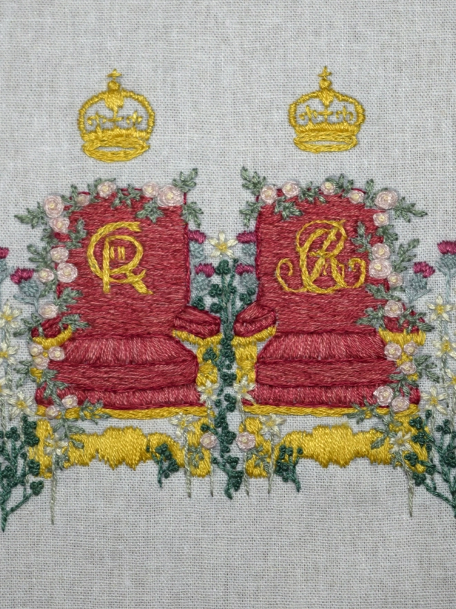 A pair of crimson chairs of estate with the cyphers of King Charles III & Queen Camila.  Surrounded by 4 nations flowers.