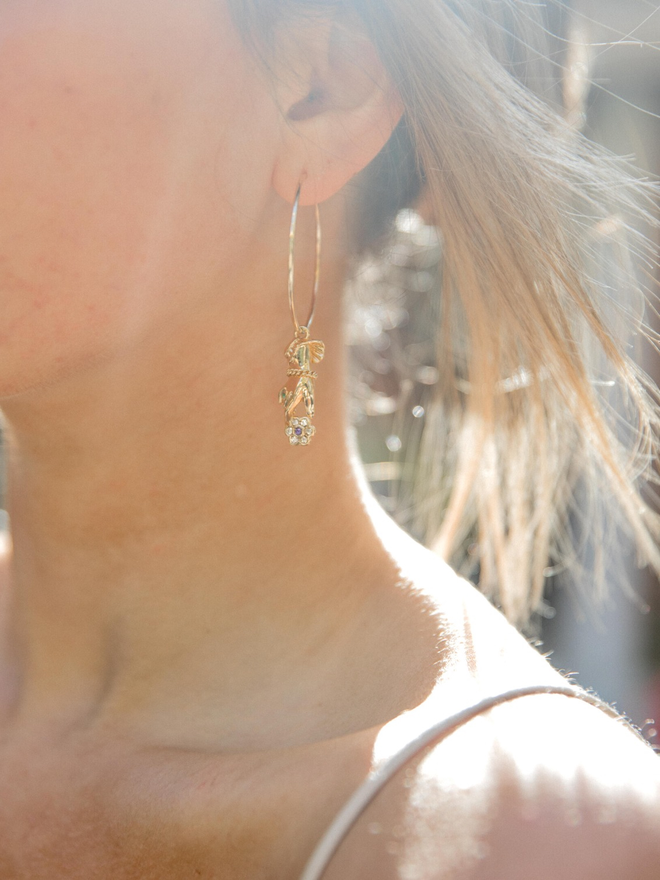 Close up of woman's ear wearing a gold hoop earring with an Emmeline Pankhurst hand charm hanging from it