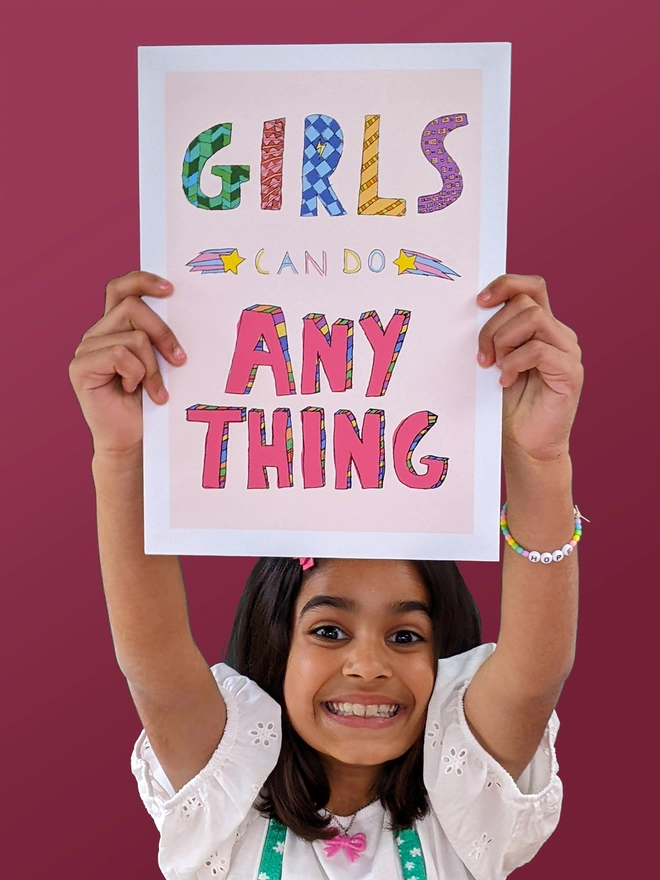 Young girl standing holding an art print saying 'Girls can do anything'