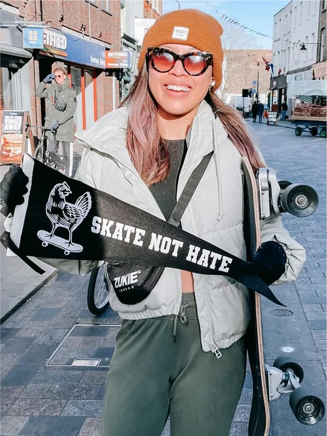 a girl skateboarder holding a black and white pennant, there is a picture of a chicken on a skateboard and the words read skate not hate