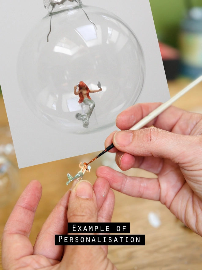 A person painting a miniature mermaid figurine to show the personaliation of hair colur 