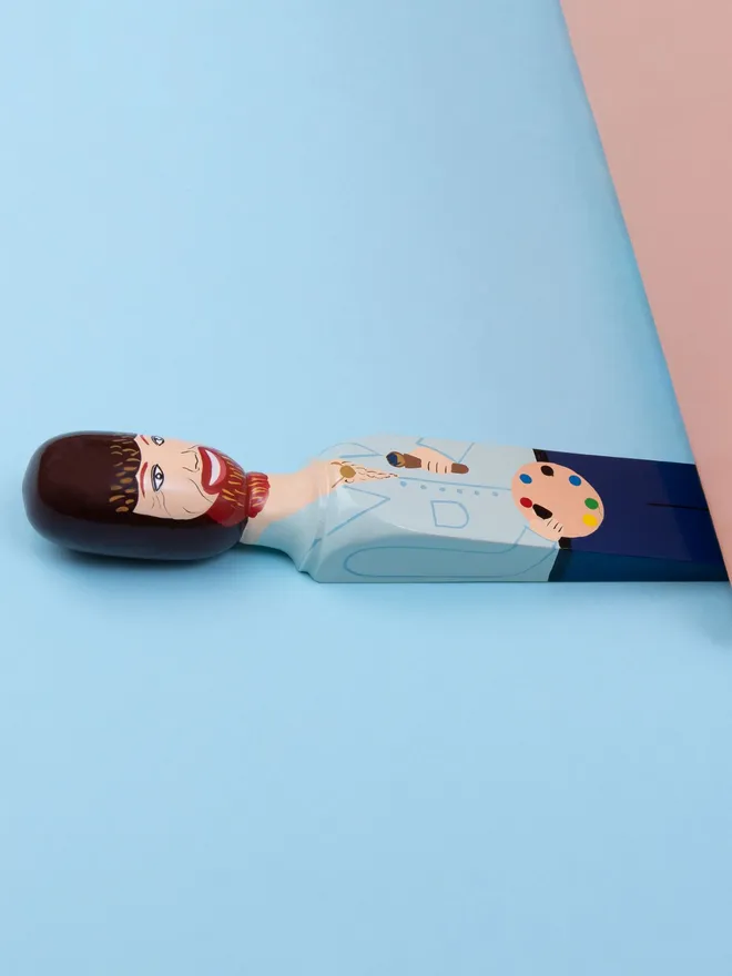 Wooden Door Stopper (Bobb), a colourful wooden door stop sitting under a door.