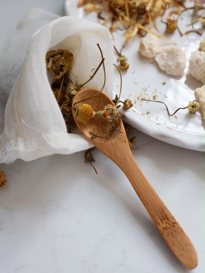 Natural, dried chamomile flowers and bamboo mixing spoon to create bath tea potions. 