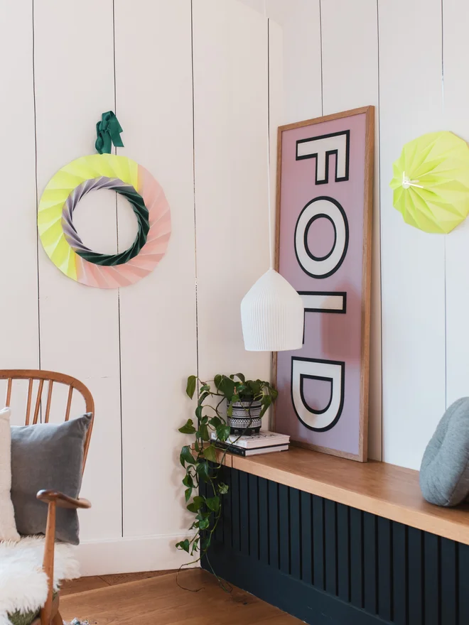 The nook of a scandinavian inspired style home, with a modern origami wreath hanging in neon yellow, pale pink, lilac and green.