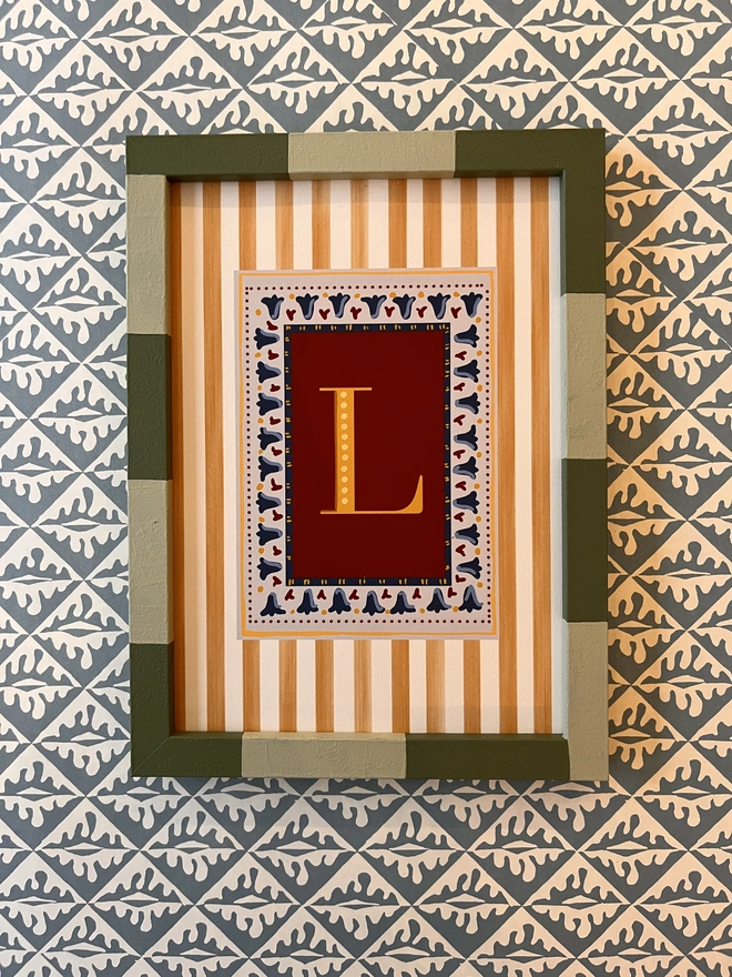 A collection of colourful hand painted bobbin and striped frames with letter prints inside surrounded by a striped border. Colourful wall art display by annabel wond interiors. 
