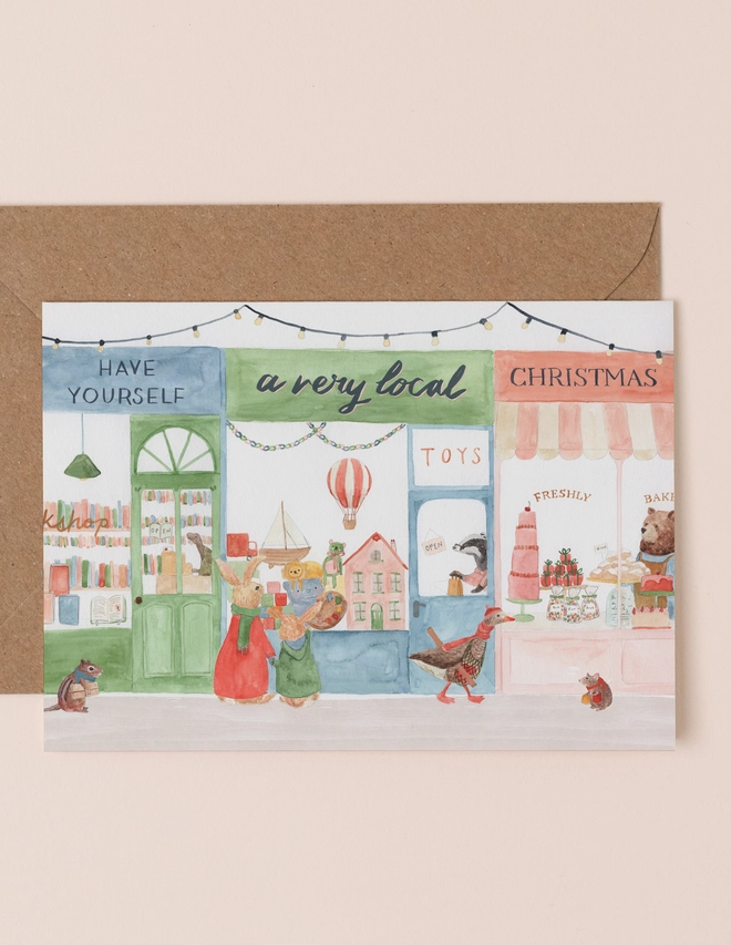 A Christmas card with an illustration of a local high street with animal shoppers and manilla envelope