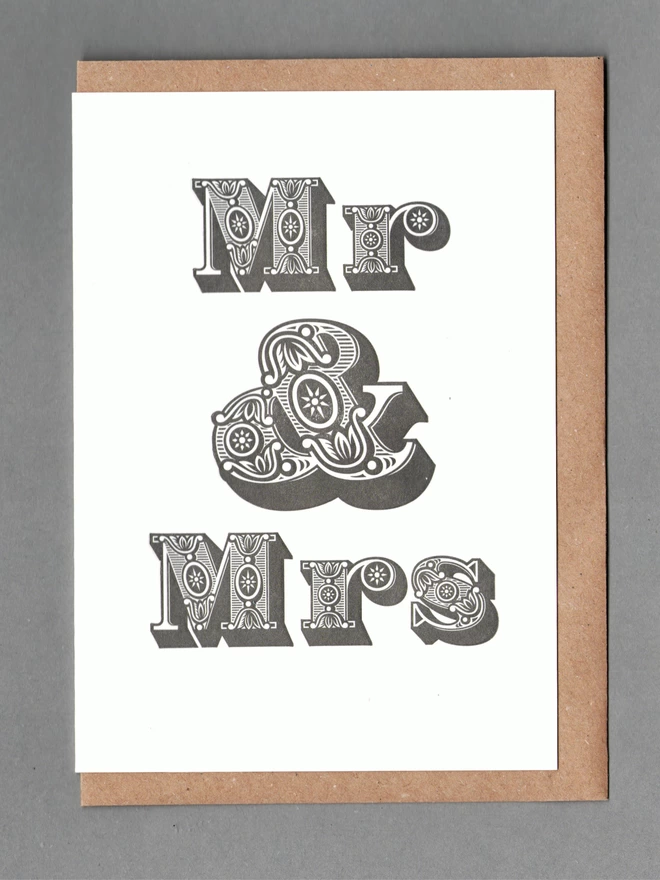 White card with black text reading 'Mr & Mrs' with a kraft envelope behind it