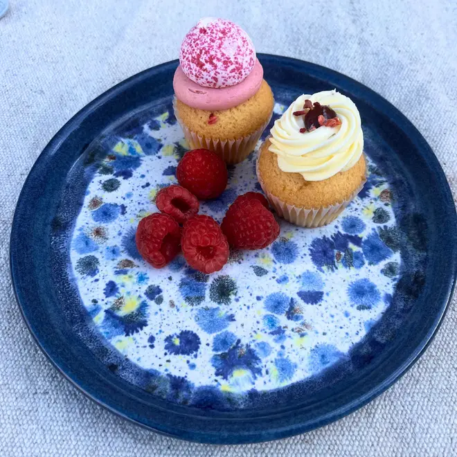 Shoreline Side Plate, a colourful plate placed on a stone surface. It is accompanied by fruits and a sweet treat. 