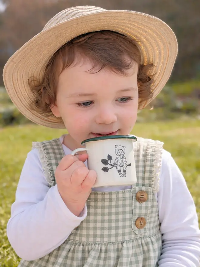a photograph of a child drinking from a sweet vintage style crean enamel mug etched with a cute pixie child wearing a wolf mug