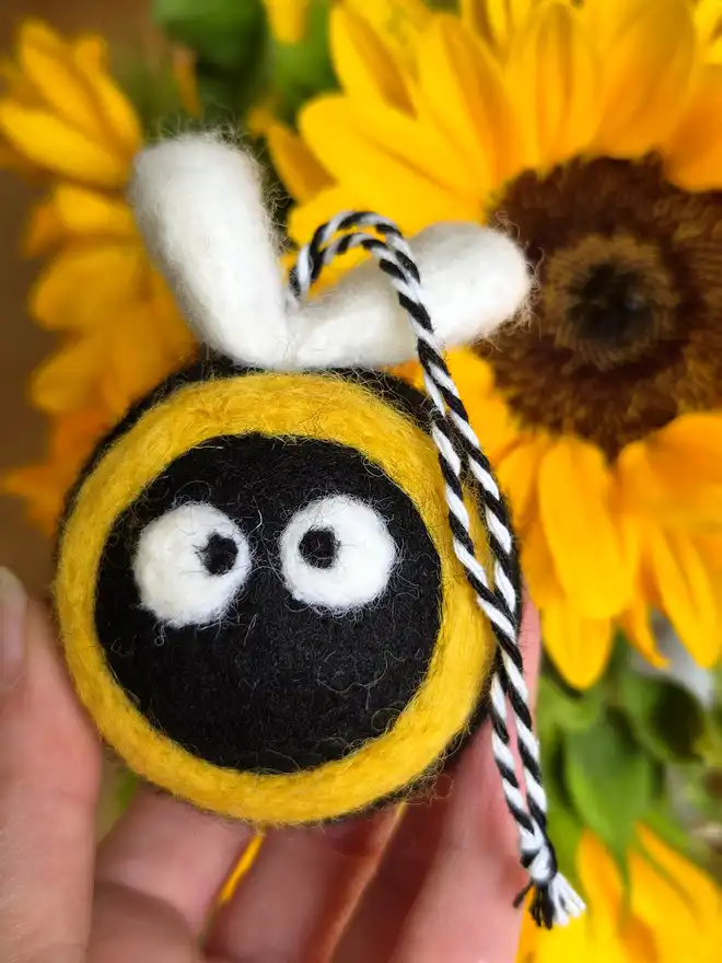 Felt Bumble Bee held in front of a vase of Sunflowers.