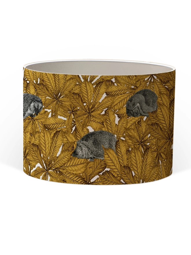 Handmade lampshade featuring cosy hedgehogs nestled among autumnal yellow leaves, creating a warm and whimsical woodland design.