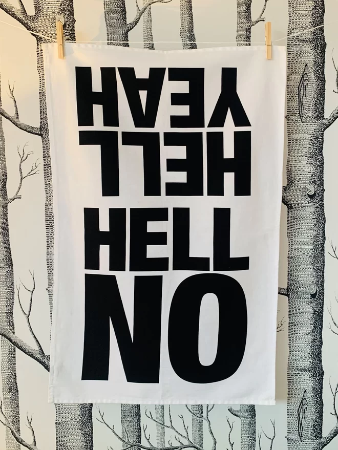 Hell yeah Hell No black screen printed text on white tea towel hanging washing line style with clothes pegs in front of white wallpaper with black trees screen print pattern of silver birch trees. Hell No facing forward . Hell Yeah reads upside down,