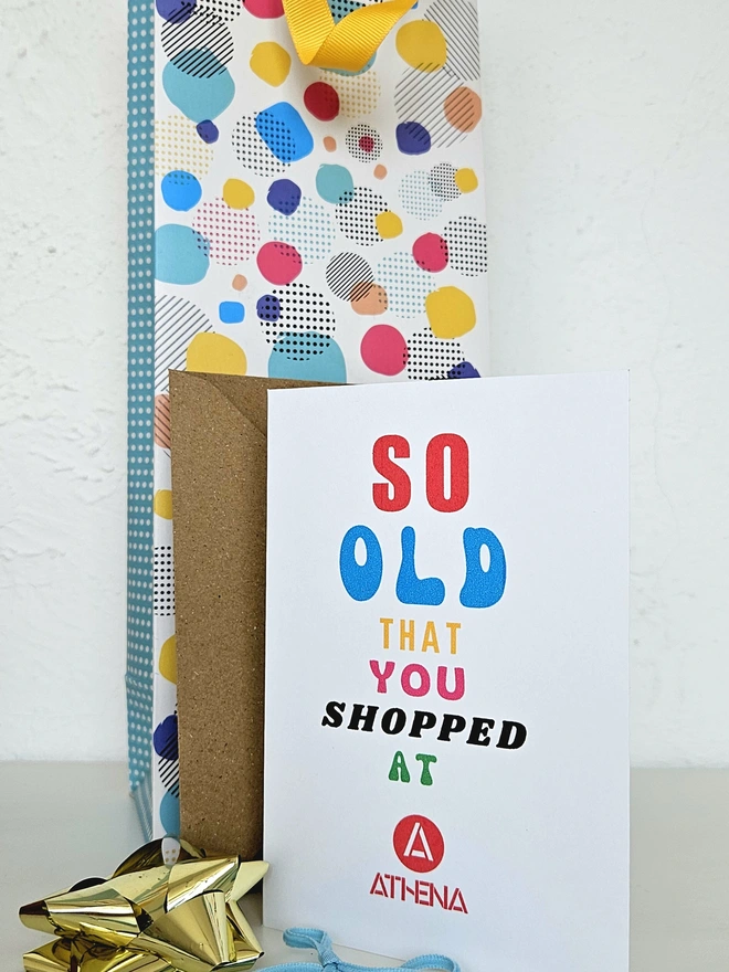 A photograph of the front of a humorous A6 greeting card illustrated using brightly coloured text and the retro shop logo. The text says so old you shopped at Athena.
