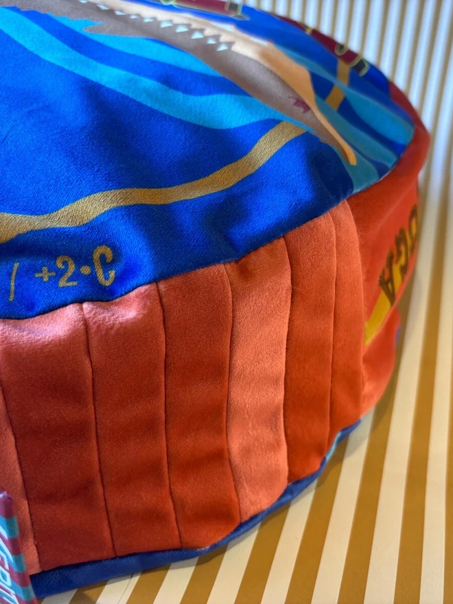 Caviar Tin Cushion, a colourful cushion with a caviar design on it. It sits on a decorated backdrop. 