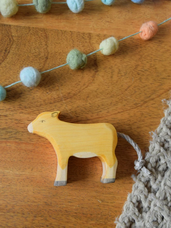 wooden toy jersey calf placed flat on table with blanket and pom pom garland