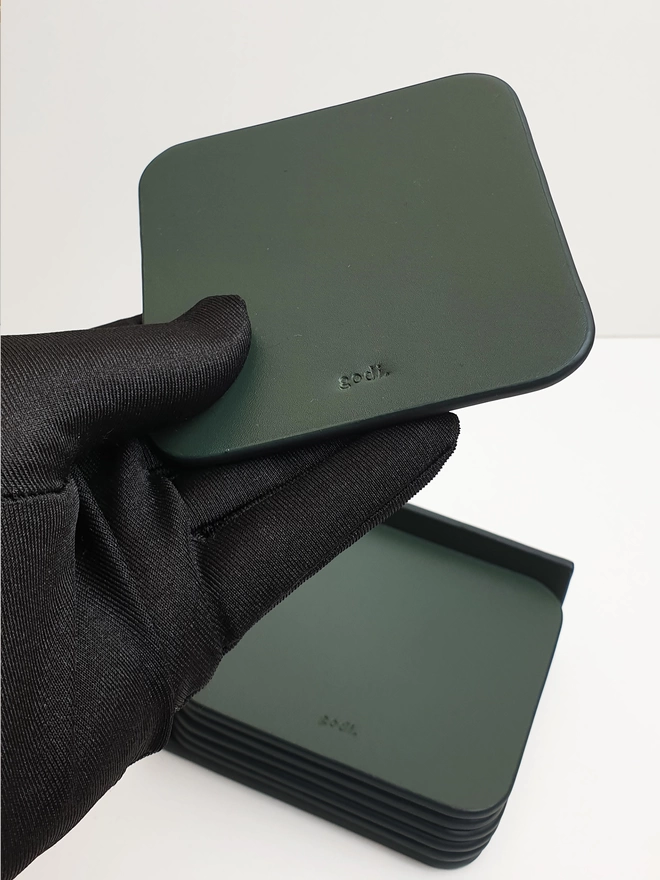 Dark Green Leather Coaster held in hand with a black glove on