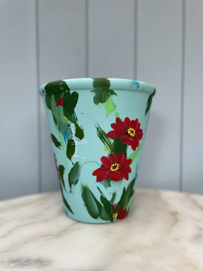 Unique hand-painted terracotta pot featuring vibrant red zinnias on a light blue background