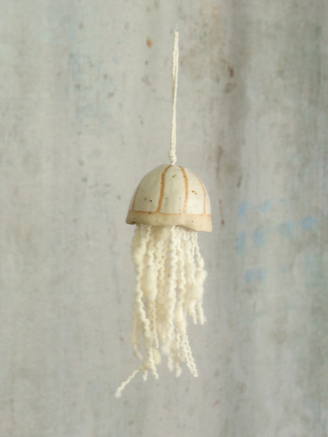 white ceramic jellyfish with wool tenticles hangs infront of an aged blue grey background