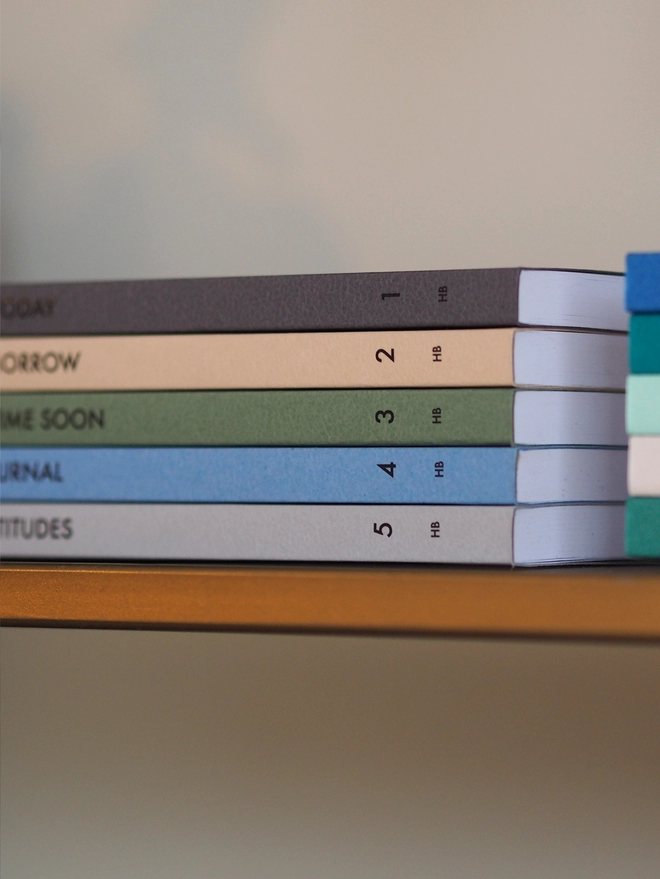 a stack of notebooks in a gradient of colours with personalised text on the spine