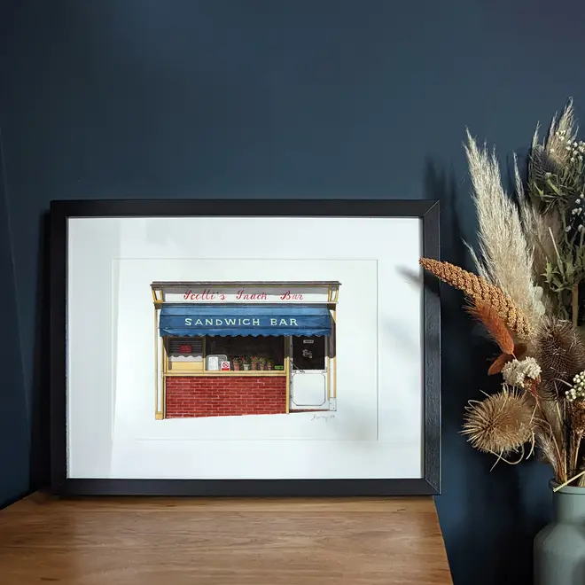 Clerkenwell Scotti's Snack Bar Giclée Print (Unframed), a print of a snack bar sitting on a wooden surface against a navy blue backdrop. It is accompanied by some flowers. 