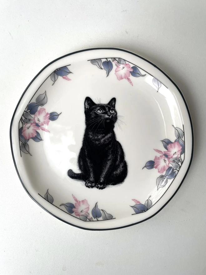 a vintage plate with an ornate border, in the centre of the plate is a vintage style black and white illustration of a black witch's cat