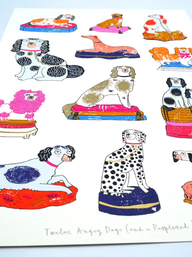 Staffordshire Pottery Dogs Screenprint Twelve Angry Dogs, a collection of colourful dog designs on a white screenprint. It sits against a baby blue backdrop. 
