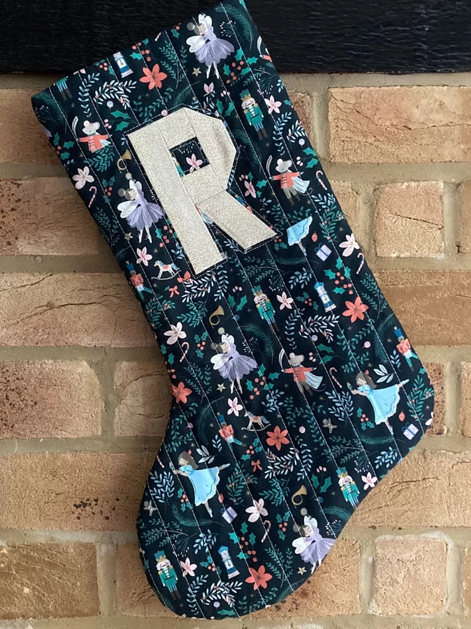 Cooper & Fred Sugar Plum Quilted Christmas Stocking with the letter 'R' in gold seen hanging on a fireplace.