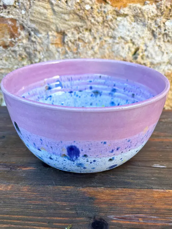 Shoreline Small Bowl, a colourful bowl placed on a wooden surface in front of a brick wall. 