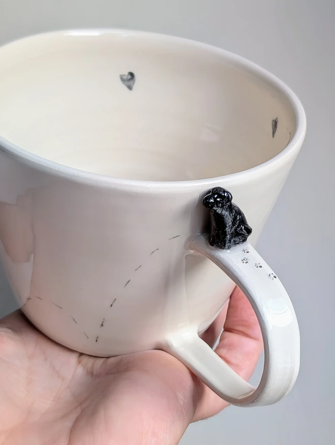 Black Labrador sculpture on the handle of an off white ceramic cup with tiny pawprints and hearts 