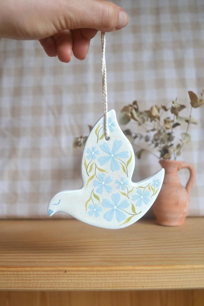white ceramic hanging bird with blue and green floral designs, in front of gingham 