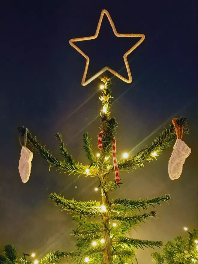 A small Christmas tree in a steel bucket, topped with a gold string covered wire star against a grey wall