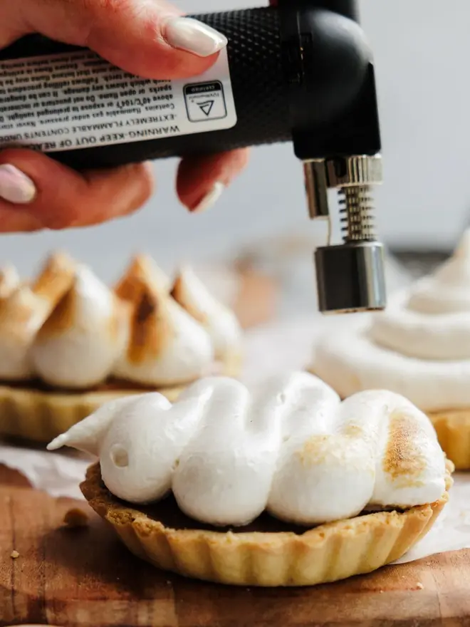 Vanilla Wonder Fluff Tub, the fluff being cooked on top of a small cookie. This is on a wooden table near more sweet treats. 