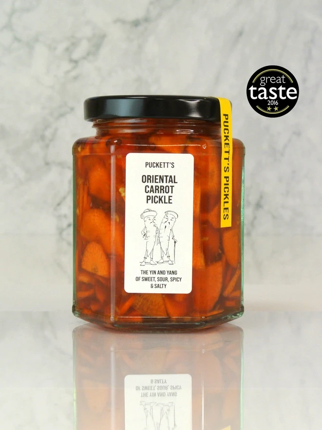 oriental carrot pickle. a jar of pickled carrot slices photographed against a marble background.